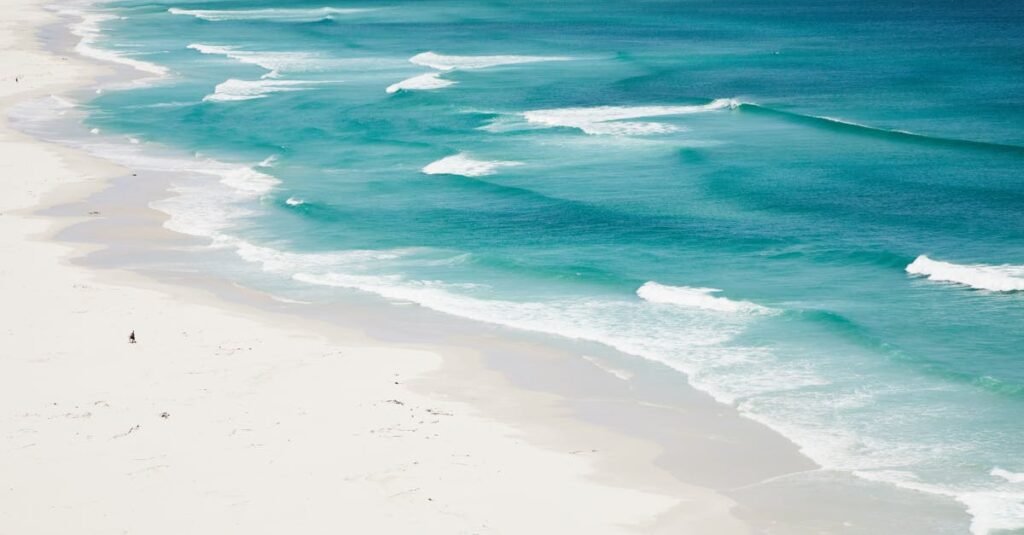 INICIO A serene aerial view of turquoise ocean waves gently washing over a pristine white sandy beach.